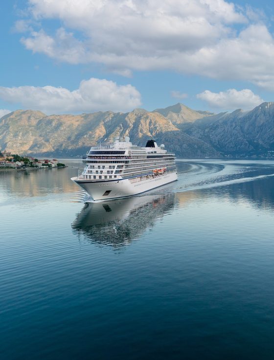 A cruise ship sailing on calm water below mountains