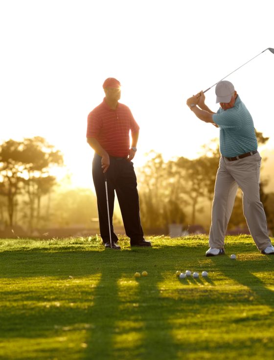 Two golfers on a fairway at sunset, one playing a shot
